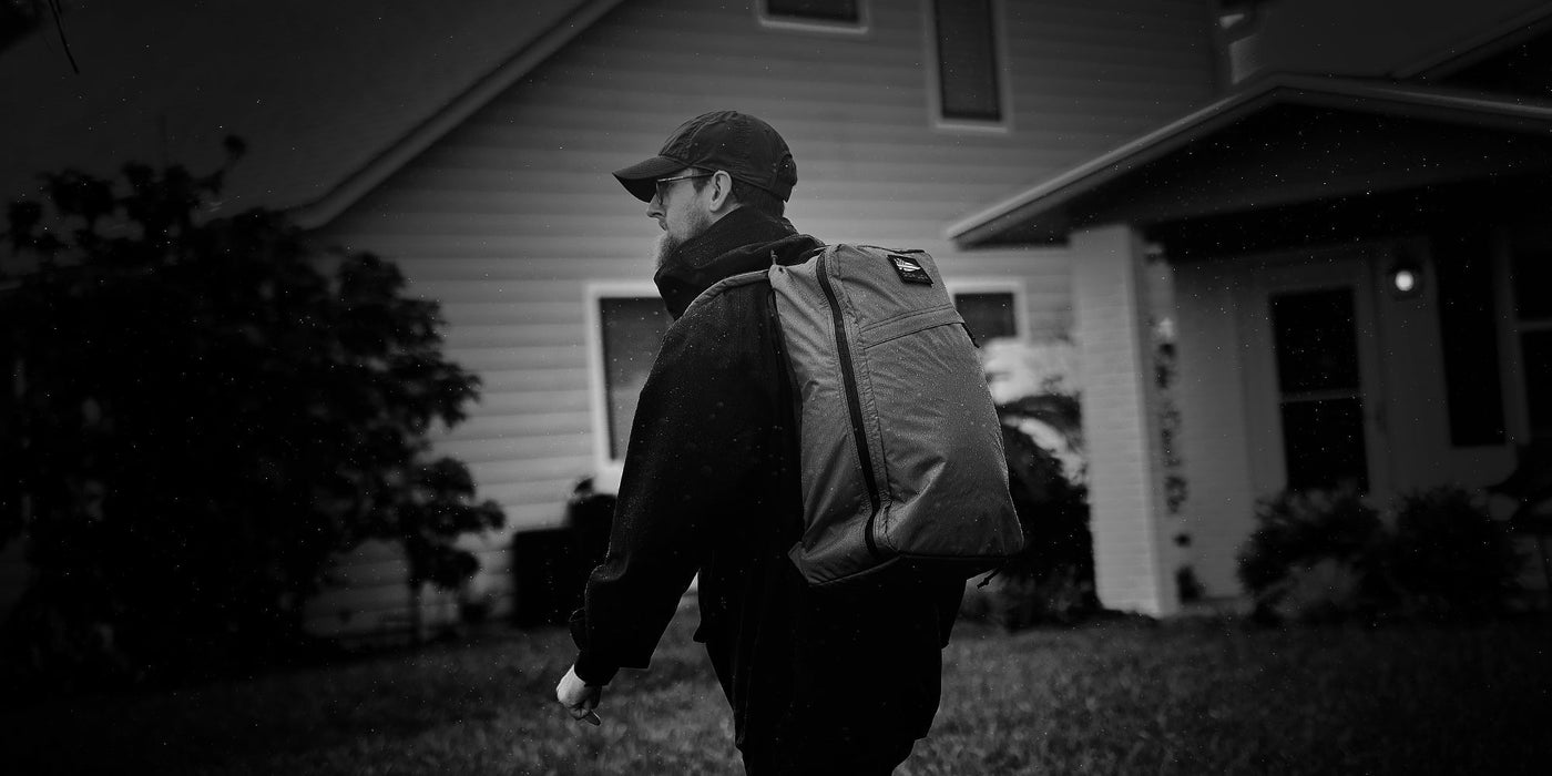 Person walking through a flooded path in a park, wearing a backpack, cap, and shorts.