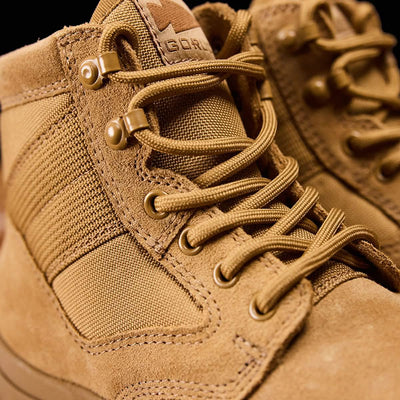 Close-up of tan-colored MACV-2 Safety Boot - Mid Top by GORUCK, featuring detailed stitching and metal eyelets for laces. These boots are designed with a rugged look, reinforced fabric, and a suede-like texture, meeting Special Forces Standards and perfect for outdoor activities.