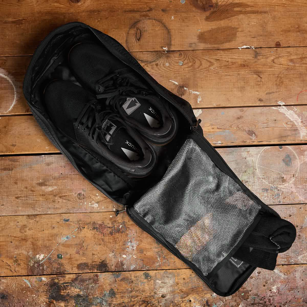 A pair of black sneakers sits inside the Shoe Bag - Ripstop ROBIC®, a water-resistant bag crafted from durable ripstop nylon, on a worn wooden surface.