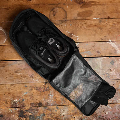 A pair of black sneakers sits inside the Shoe Bag - Ripstop ROBIC®, a water-resistant bag crafted from durable ripstop nylon, on a worn wooden surface.