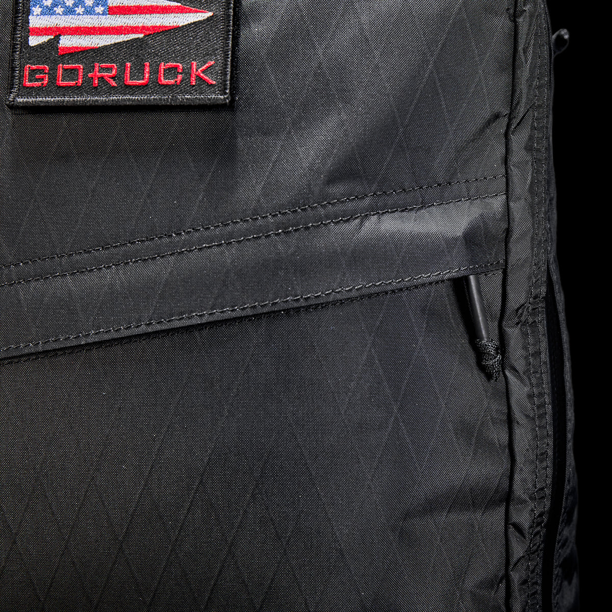 Close-up of the GR1 USA - X-PAC, a black GORUCK rucksack made from durable X-PAC® material, with a USA flag patch on the front.