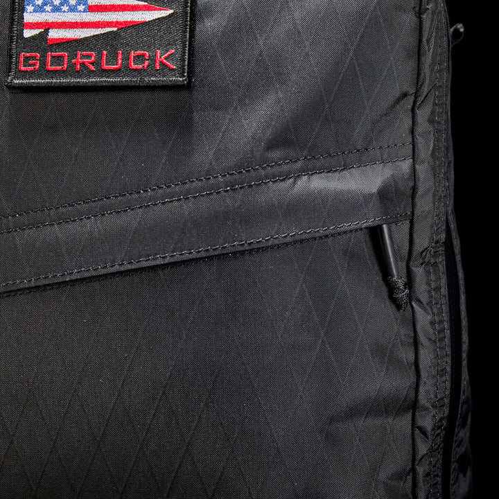 Close-up of the GR1 USA - X-PAC, a black GORUCK rucksack made from durable X-PAC® material, with a USA flag patch on the front.