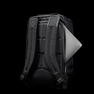 The GR1 USA - X-PAC rucksack showcases a sleek black design with a laptop partially visible in the back pocket, set against a black background, blending durability with style.
