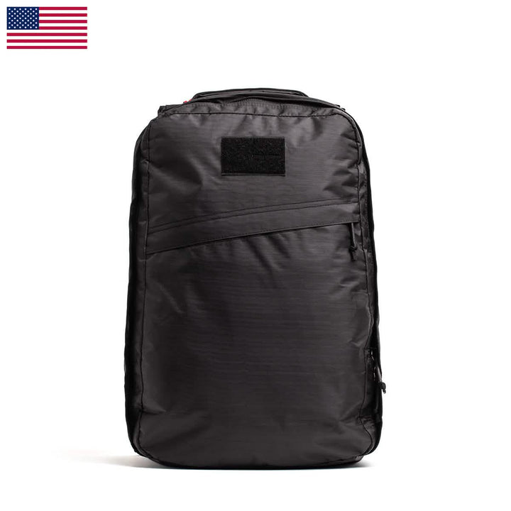 The GR1 USA - Dyneema by GORUCK is a black rucksack with a minimalist design, showcasing a zipper pocket on the front and a rectangular patch area. Constructed from durable Dyneema®, it features an American flag icon in the top left corner, reminiscent of the classic GR1 style.