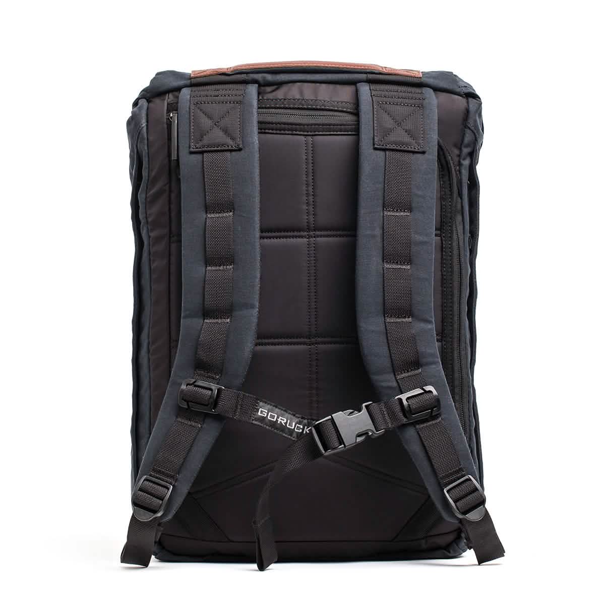 The GORUCK M23 - Waxed Canvas is a black, military-inspired backpack featuring padded shoulder straps and an adjustable chest buckle. Its back panel is designed with thick cushioning for enhanced comfort, while the brand's name is prominently displayed near the buckle area.