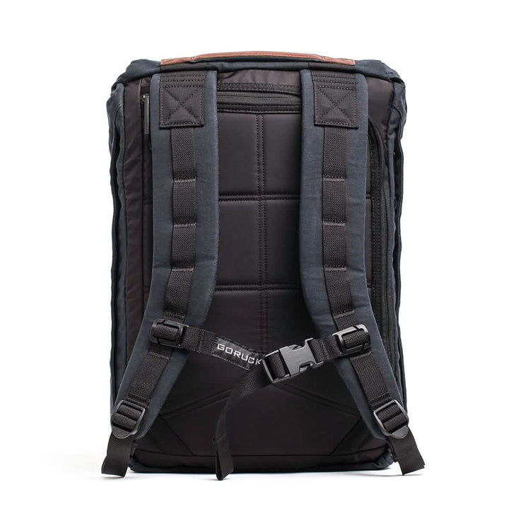 The GORUCK M23 - Waxed Canvas is a black, military-inspired backpack featuring padded shoulder straps and an adjustable chest buckle. Its back panel is designed with thick cushioning for enhanced comfort, while the brand's name is prominently displayed near the buckle area.