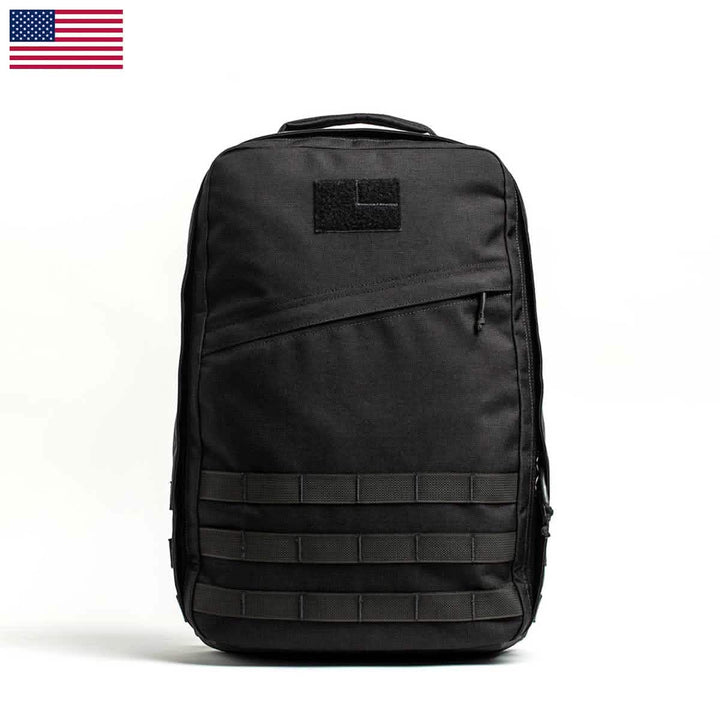 The GR1 USA - Cordura by GORUCK is a black tactical backpack known for its Special Forces grade durability. It features MOLLE webbing, a patch area, and an American flag graphic in the corner. The backpack includes a bombproof laptop compartment for enhanced security.