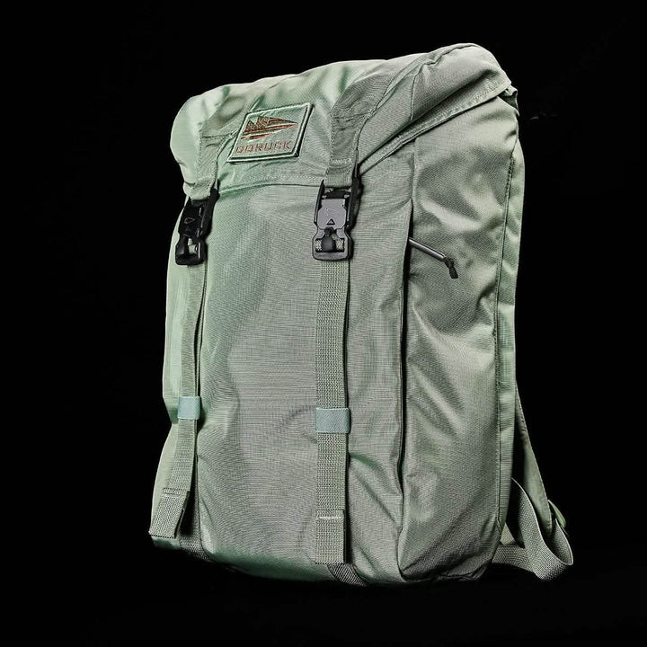 The M23 - Ripstop ROBIC® rucksack by GORUCK, in Seaspray + Speed Tan, is designed with a top flap and two buckle closures. Made from durable materials, it features a rectangular patch with text and adjustable shoulder straps. Its black background enhances the backpack's appearance perfectly.