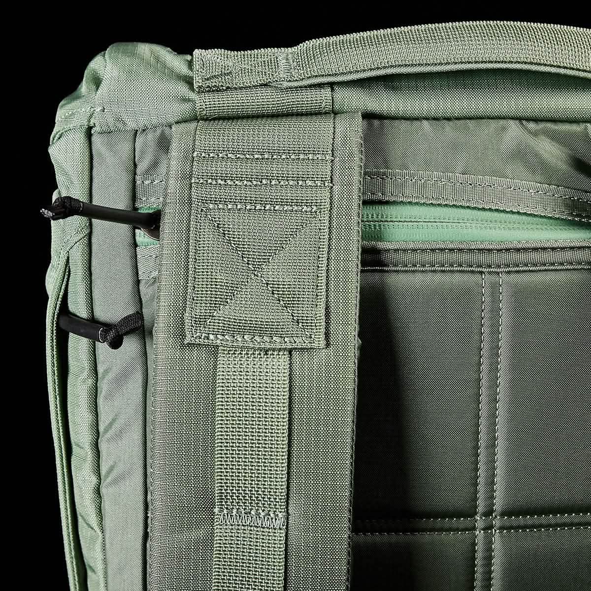 Close-up of a GORUCK M23 - Ripstop ROBIC® rucksack in Seaspray and Speed Tan, highlighting a zippered compartment, two black corded loops, and reinforced stitching. The emphasis is on the durable materials and functional design elements that ensure this field pack's reliability in any situation.