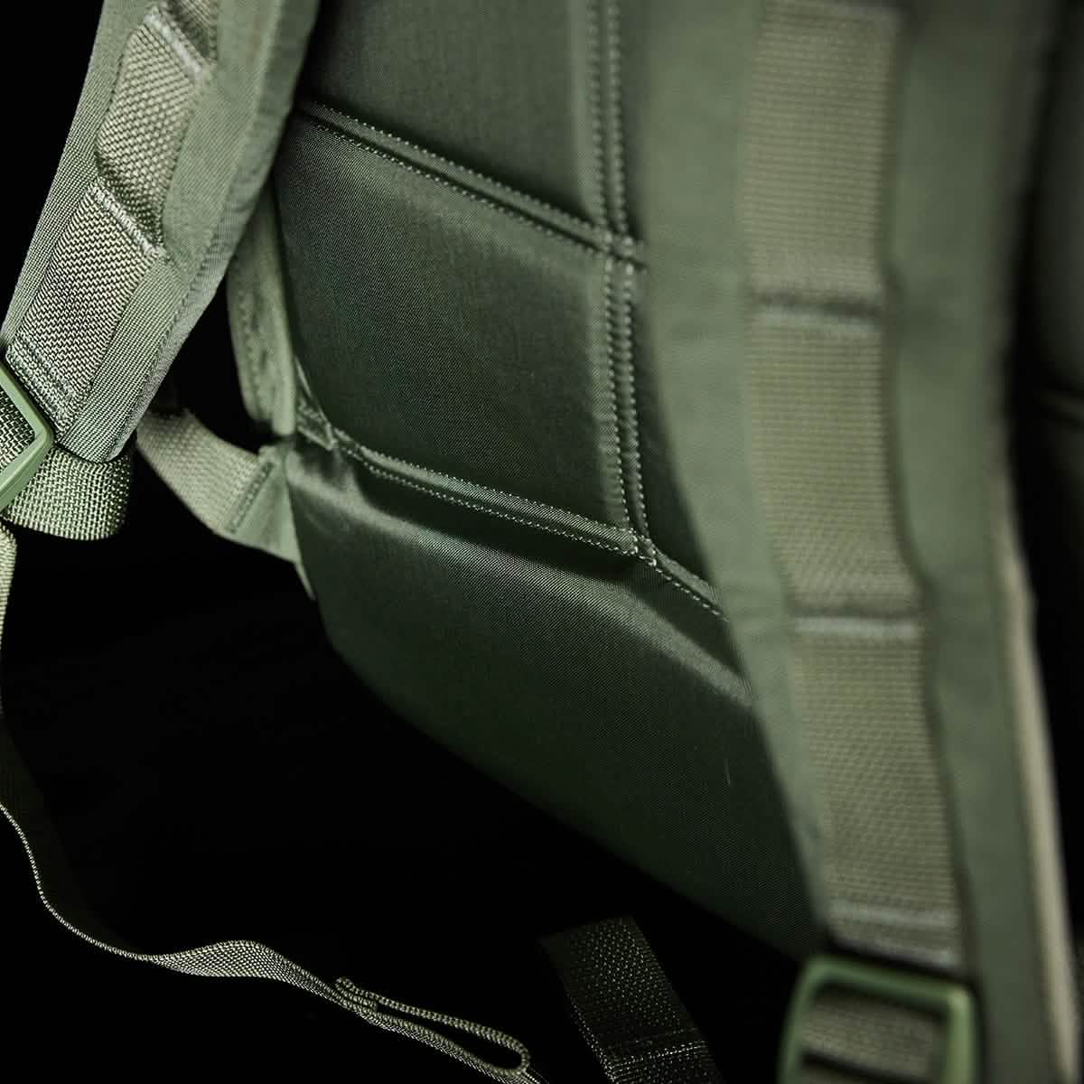 The close-up of the olive green GORUCK KR1 kids rucksack emphasizes its durable fabric and stitching, complemented by a padded back and adjustable straps, perfectly suited for carrying school supplies comfortably against a dark background.