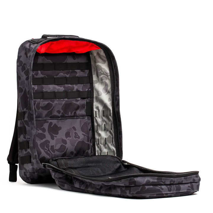 A GORUCK GR2-style gray camouflage ruck showcases a vivid red interior lining. Its open layout displays several compartments and black straps, reminiscent of the organized efficiency found in Special Forces equipment.