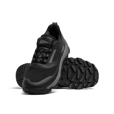 Introducing the Mackall - Black + Forged Iron trail shoes by GORUCK, featuring thick, rugged soles ideal for rucking. One shoe stands upright facing forward, while the other is tilted to showcase its textured sole. Set against a plain white background, these shoes are designed to conquer any terrain or challenge.