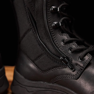 A close-up of the GORUCK MACV-2 Safety Boot - High Top, designed to meet Special Forces standards, highlights its detailed stitching, side zipper, and robust laces. The black boot's durable material with a sleek finish makes it ideal for rugged use. It is positioned on a wooden surface.