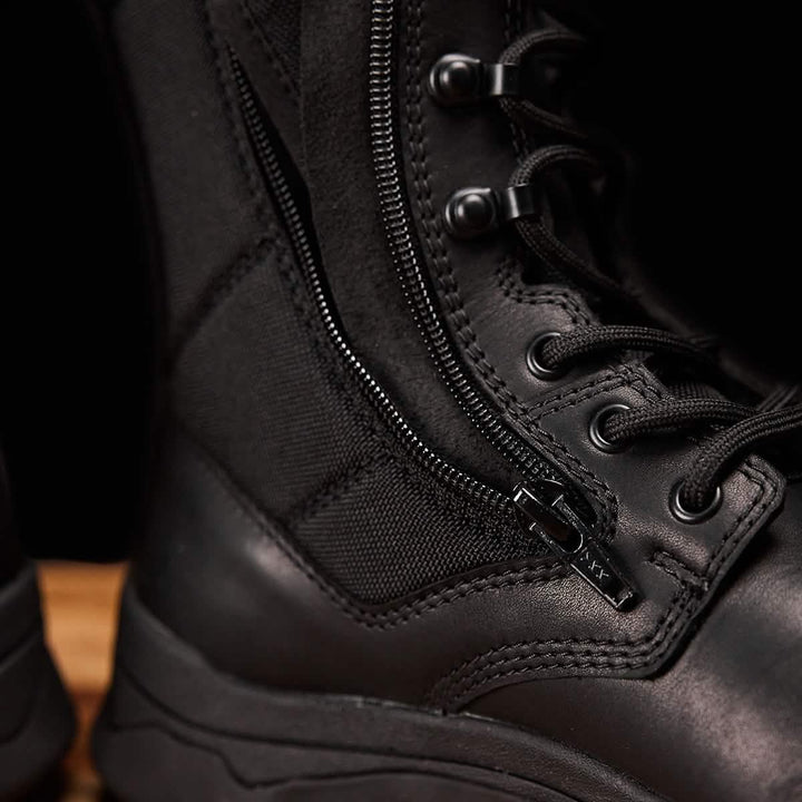 A close-up of the GORUCK MACV-2 Safety Boot - High Top, designed to meet Special Forces standards, highlights its detailed stitching, side zipper, and robust laces. The black boot's durable material with a sleek finish makes it ideal for rugged use. It is positioned on a wooden surface.