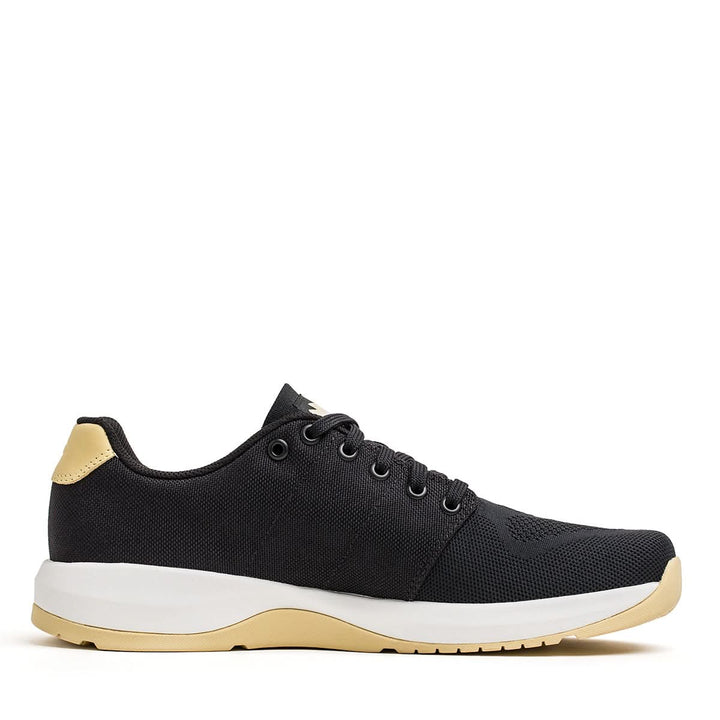 Introducing the Women's Ballistic Trainers from GORUCK, featuring a sleek black and gold design with laces and crafted from durable CORDURA® Ballistic Nylon for exceptional strength. Boasting a white midsole, beige outsole, and 3X Support™ technology, these shoes are the ideal choice for functional fitness footwear enthusiasts.