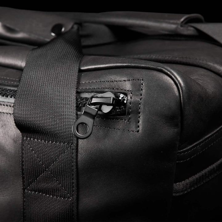 Close-up of the GORUCK Kit Bag x Carryology - Berserker Viking, featuring a textured black leather finish reminiscent of Viking armor. Highlighting the zipper pull, it is uniquely attached to a fabric strap that is expertly stitched onto the bag, showcasing craftsmanship and design elements akin to those prized by Norsemen warriors.
