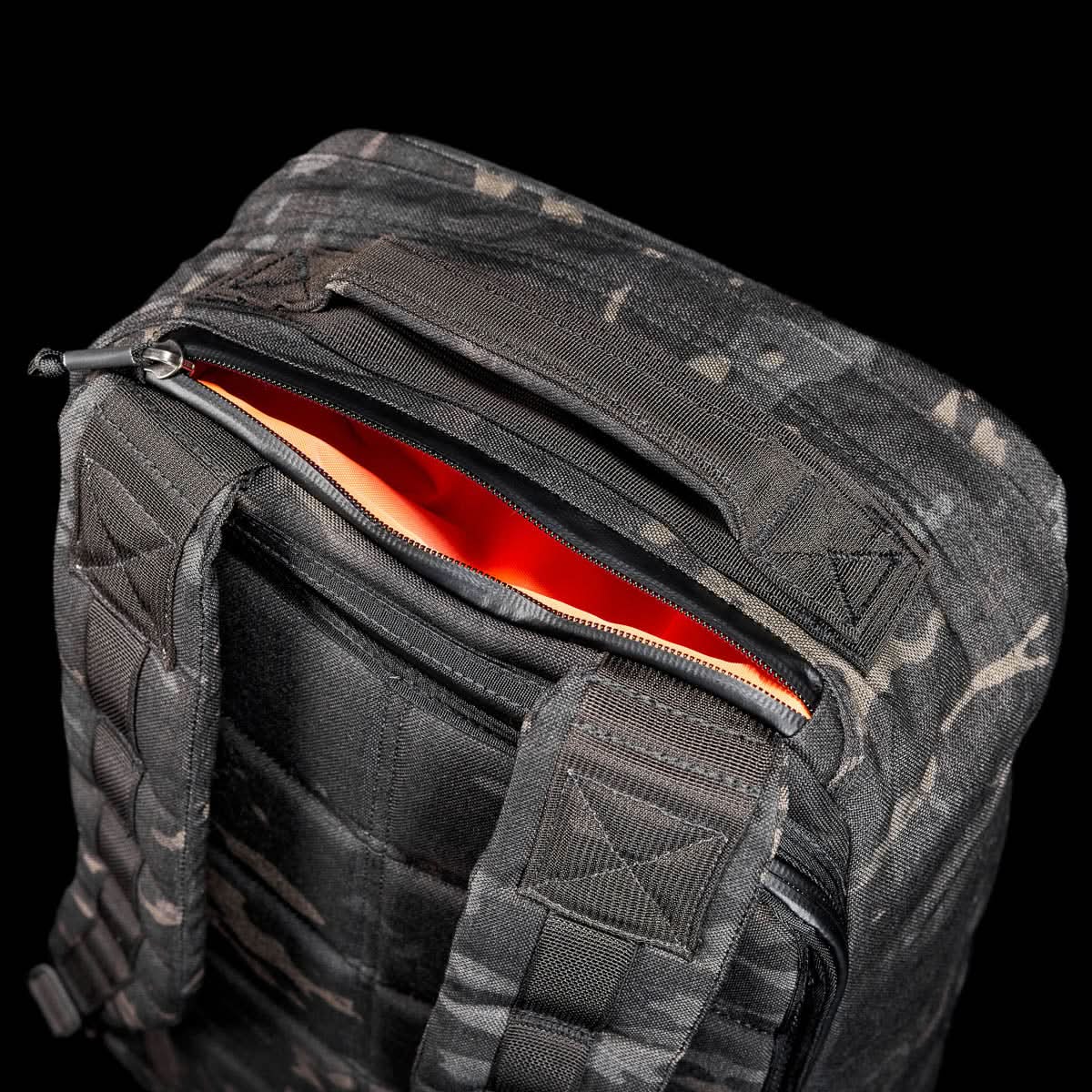 The GR1 USA - Cordura (The Original Ruck), black camo with orange lining, made from Special Forces-grade materials, is partially unzipped and displayed against a black background. Inspired by the legendary GR1 and perfect for GORUCK Challenges.