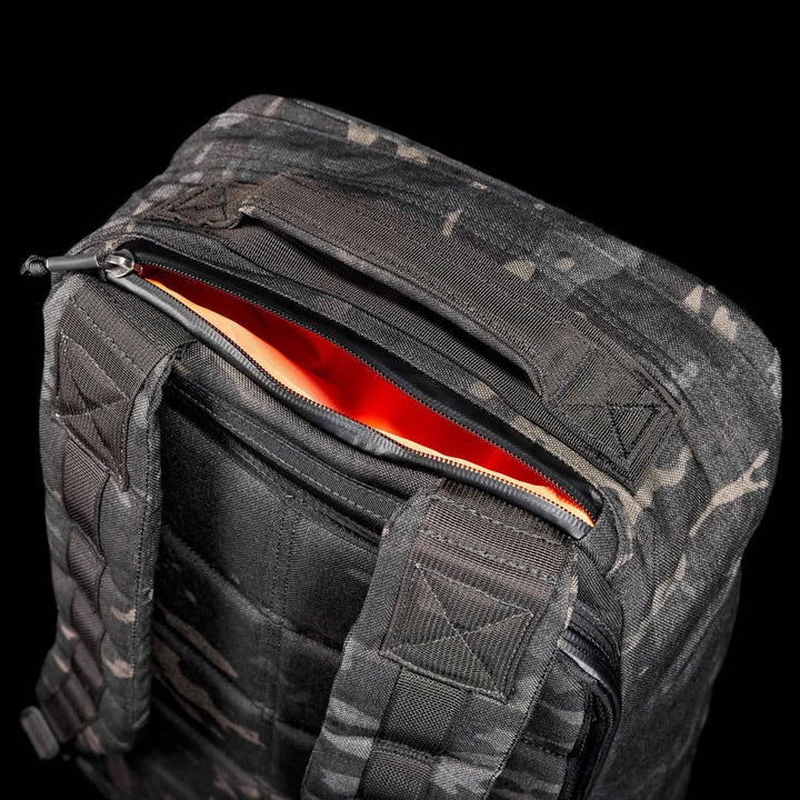 The GR1 USA - Cordura (The Original Ruck), black camo with orange lining, made from Special Forces-grade materials, is partially unzipped and displayed against a black background. Inspired by the legendary GR1 and perfect for GORUCK Challenges.