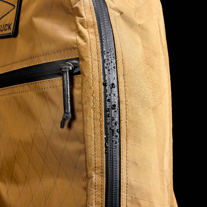 Close-up of the Bullet X-PAC brown daypack with water droplets on its black AquaGuard zippers, showcasing its water-resistant material.