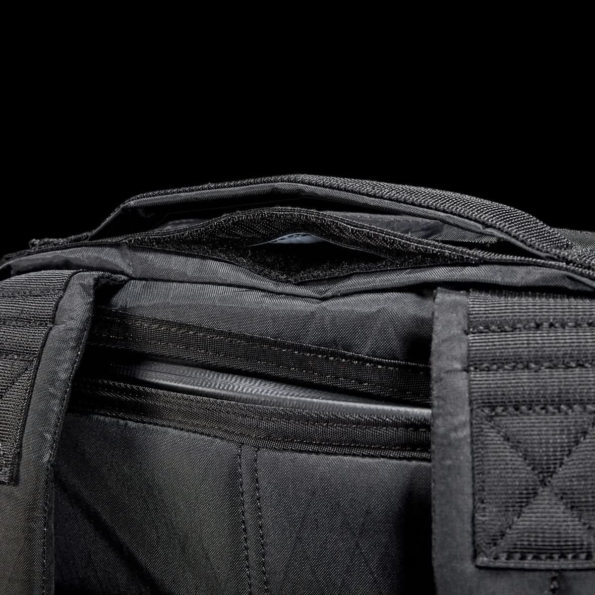 Close-up of the GR0 - X-PAC, a black waterproof fabric bag with visible zippers and handles, set against a black background.