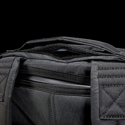 Close-up of the GR0 - X-PAC, a black waterproof fabric bag with visible zippers and handles, set against a black background.