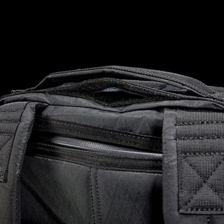 Close-up of the GR0 - X-PAC, a black waterproof fabric bag with visible zippers and handles, set against a black background.