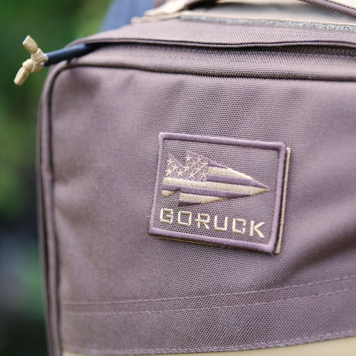Close-up of a brown Rucker 4.0 rucksack with a patch featuring an arrow and stars on the front—ideal for rucking or carrying your ruck plates in style.