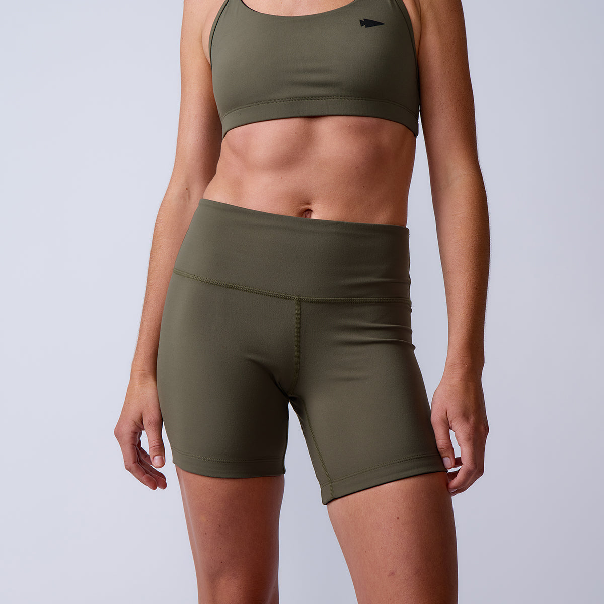 A person wearing olive green sports bra and Women’s Biker Shorts - ToughFlex stands against a plain background.