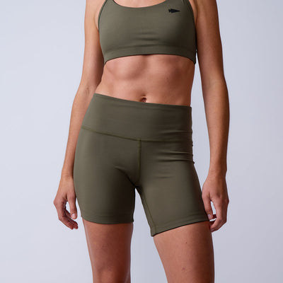 A person wearing olive green sports bra and Women’s Biker Shorts - ToughFlex stands against a plain background.