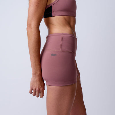A woman stands sideways against a light background in high-waisted mauve Women’s Squat Shorts - ToughFlex and a sports bra, highlighting the shorts' flexible ToughFlex fabric.