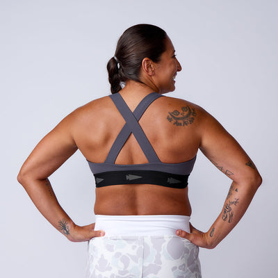 A tattooed woman is seen from the back wearing the gray Power Bra - Toughflex and white leggings, set against a plain background.