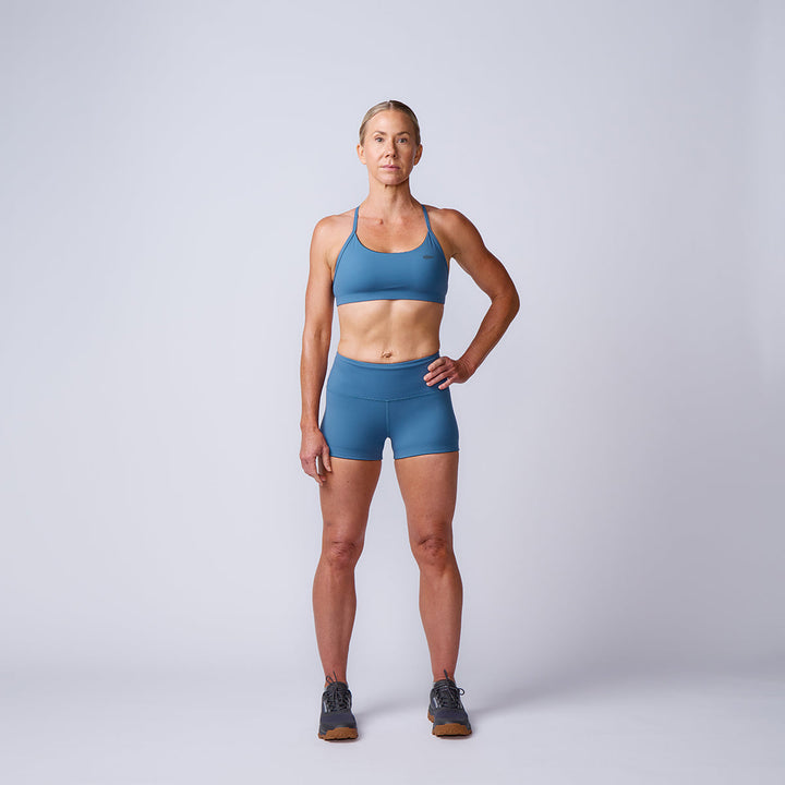 Woman in blue high-waisted sports bra and Women’s Squat Shorts - ToughFlex stands confidently against a plain light background.