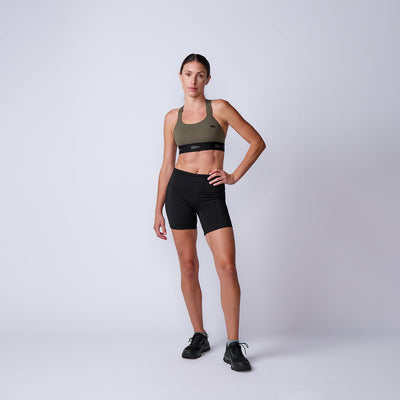 Woman in Women’s Biker Shorts - ToughFlex stands confidently against a plain light background, paired with a sports bra and sneakers.