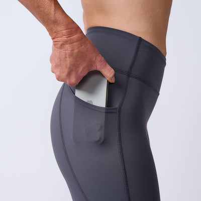A person slips a smartphone into the side pocket of dark gray Women’s Training Leggings Pocket - ToughFlex, highlighting these durable workout leggings designed for convenience.