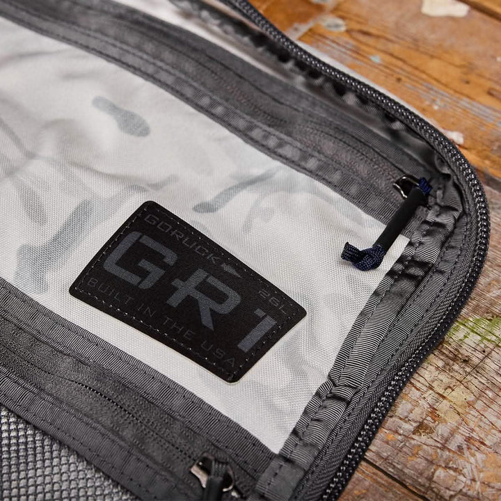 Zoom in on the interior label of the GR1 USA - Cordura (The Original Ruck) by GORUCK, showcasing its "Built in the USA" heritage, inspired by Special Forces. The gray and black design is highlighted by a prominent zipper and precise stitching, as the backpack sits on a wooden surface, poised for any GORUCK Challenge.