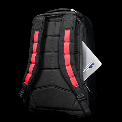 The GR1 Shooter 26L - Built by Scars backpack features red-accented straps, durable CORDURA® fabric, and a back pocket with a partially visible silver laptop.