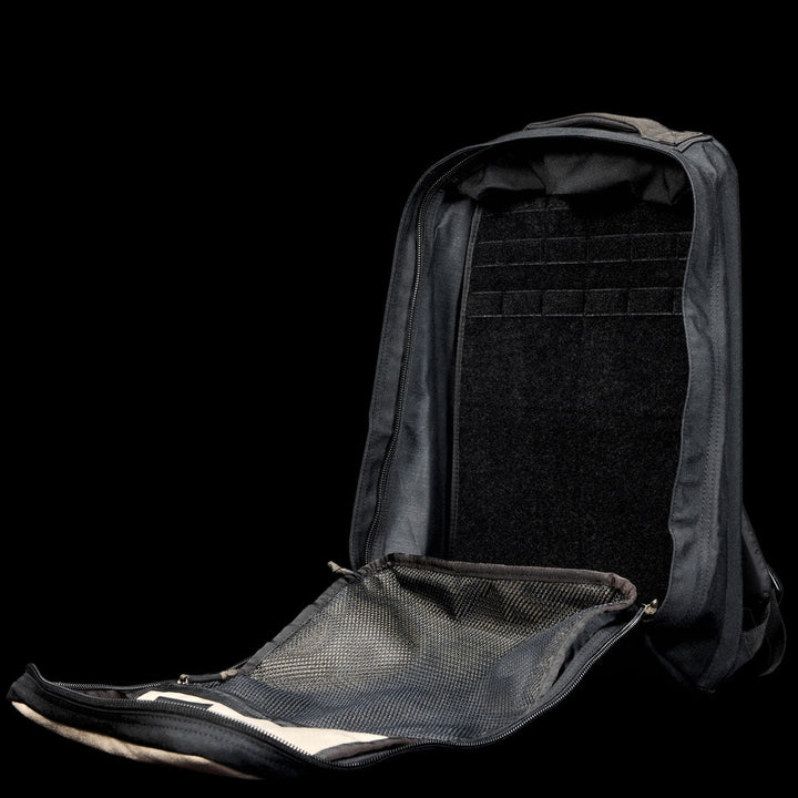 A black GR1 Shooter 26L - Built by Scars backpack, crafted from rugged CORDURA® fabric, sits open against a black background, revealing its empty main compartment and mesh pocket.