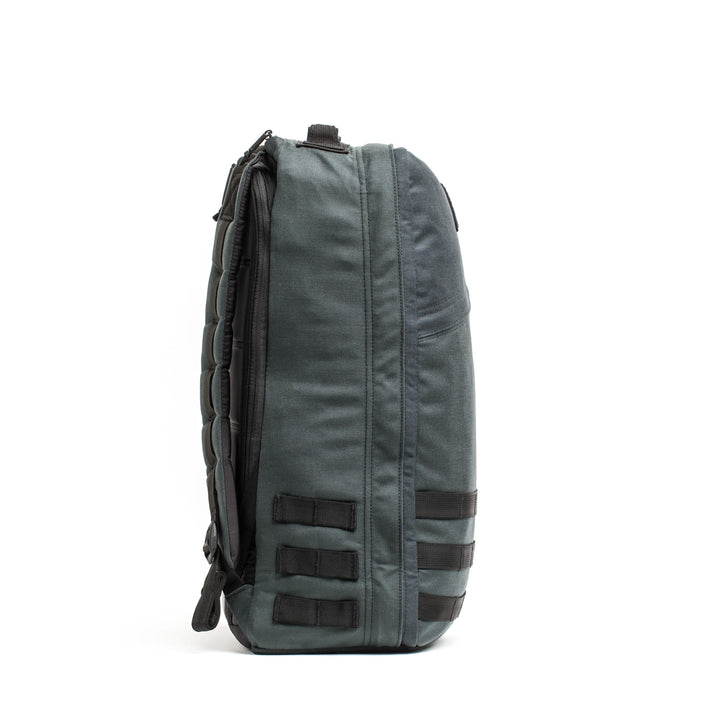 Here is a rewritten version of the sentence using the product data:

Side view of a dark gray GORUCK GR1 USA - Cordura backpack with padded straps, inspired by Special Forces requirements. It includes multiple compartments and black attachment loops on the side, standing upright against a plain white background.