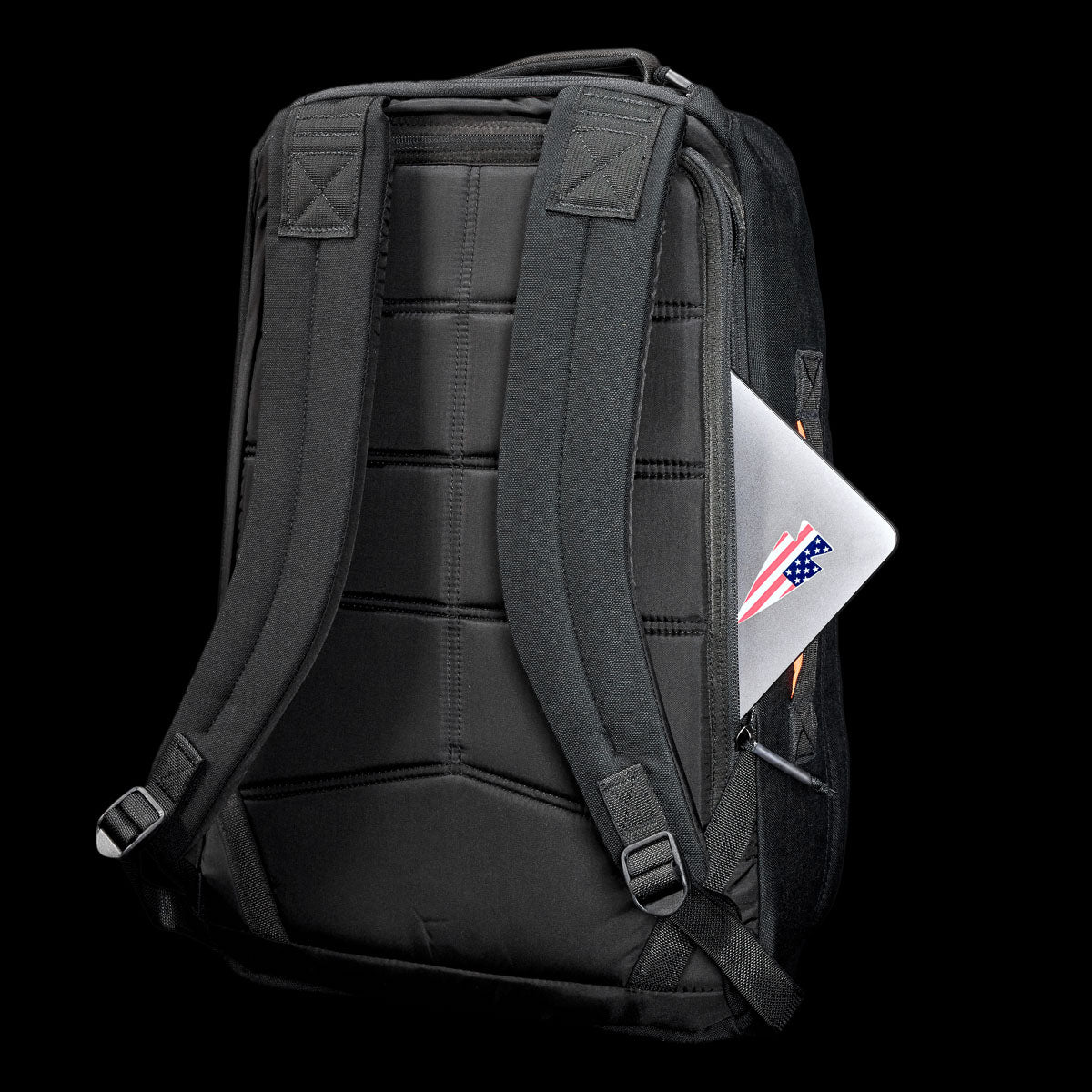 The GR1 Shooter 26L - Built by Scars backpack, crafted from Special Forces Grade CORDURA®, with visible straps, holds a laptop featuring a US flag sticker in the side pocket, all set against a black background.