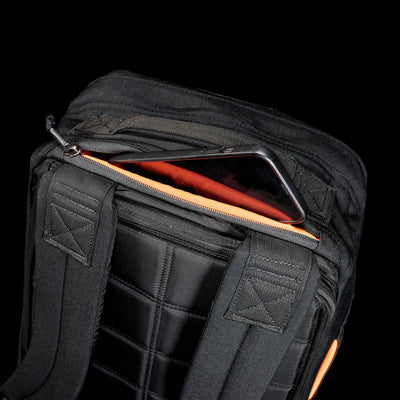 A smartphone partially tucked in a zippered pocket on a black GR1 Shooter 26L - Built by Scars backpack, crafted from Special Forces Grade CORDURA® with padded straps.