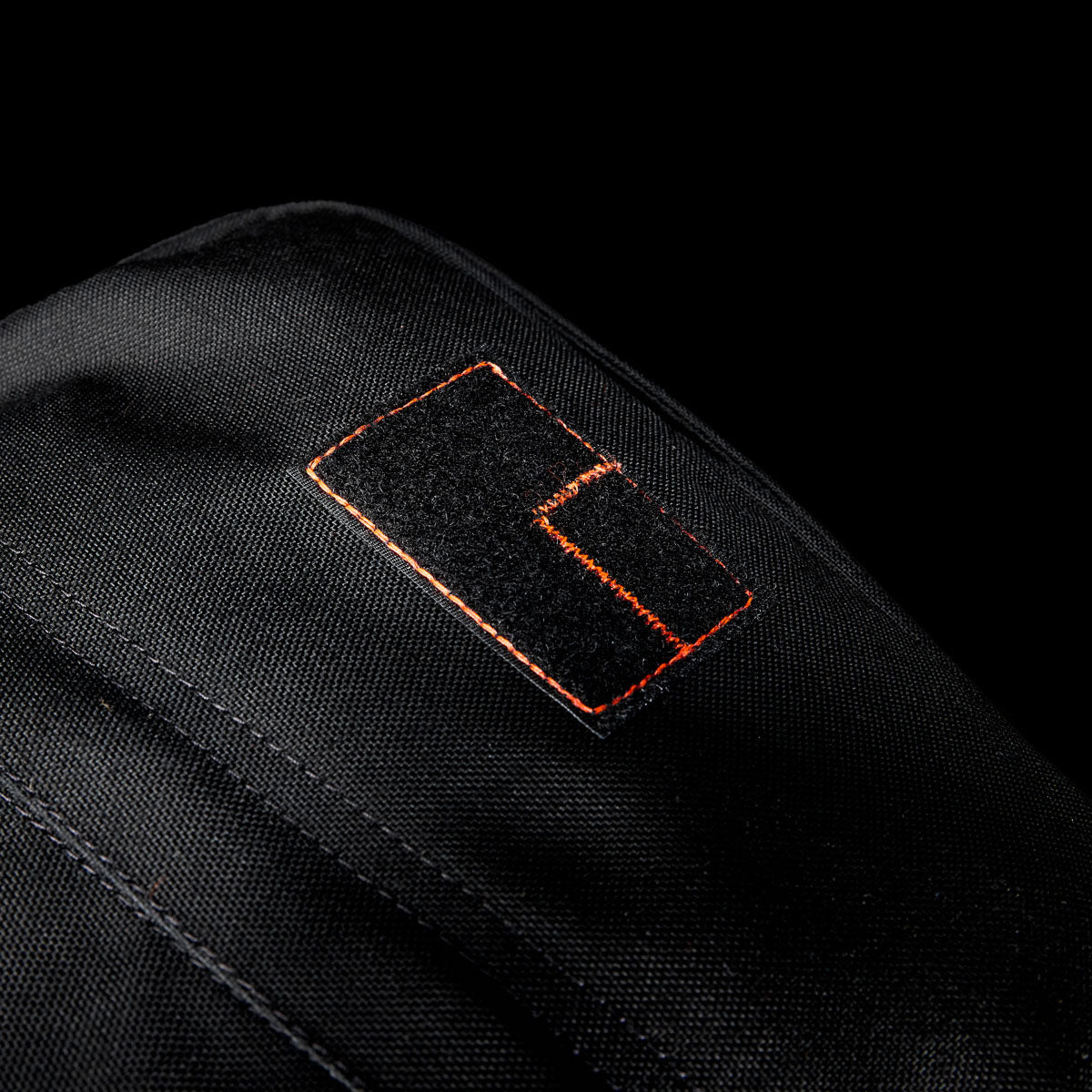 Close-up of a black Special Forces Grade CORDURA® patch with orange stitching on a black background, inspired by the legendary GR1 Shooter 26L - Built by Scars design.