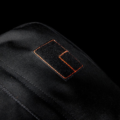 Close-up of a black Special Forces Grade CORDURA® patch with orange stitching on a black background, inspired by the legendary GR1 Shooter 26L - Built by Scars design.