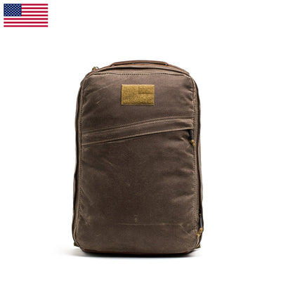 The GR1 USA - Heritage Waxed Canvas is a durable backpack made from waxed duck canvas, featuring a tan patch and a small American flag in the top left corner.