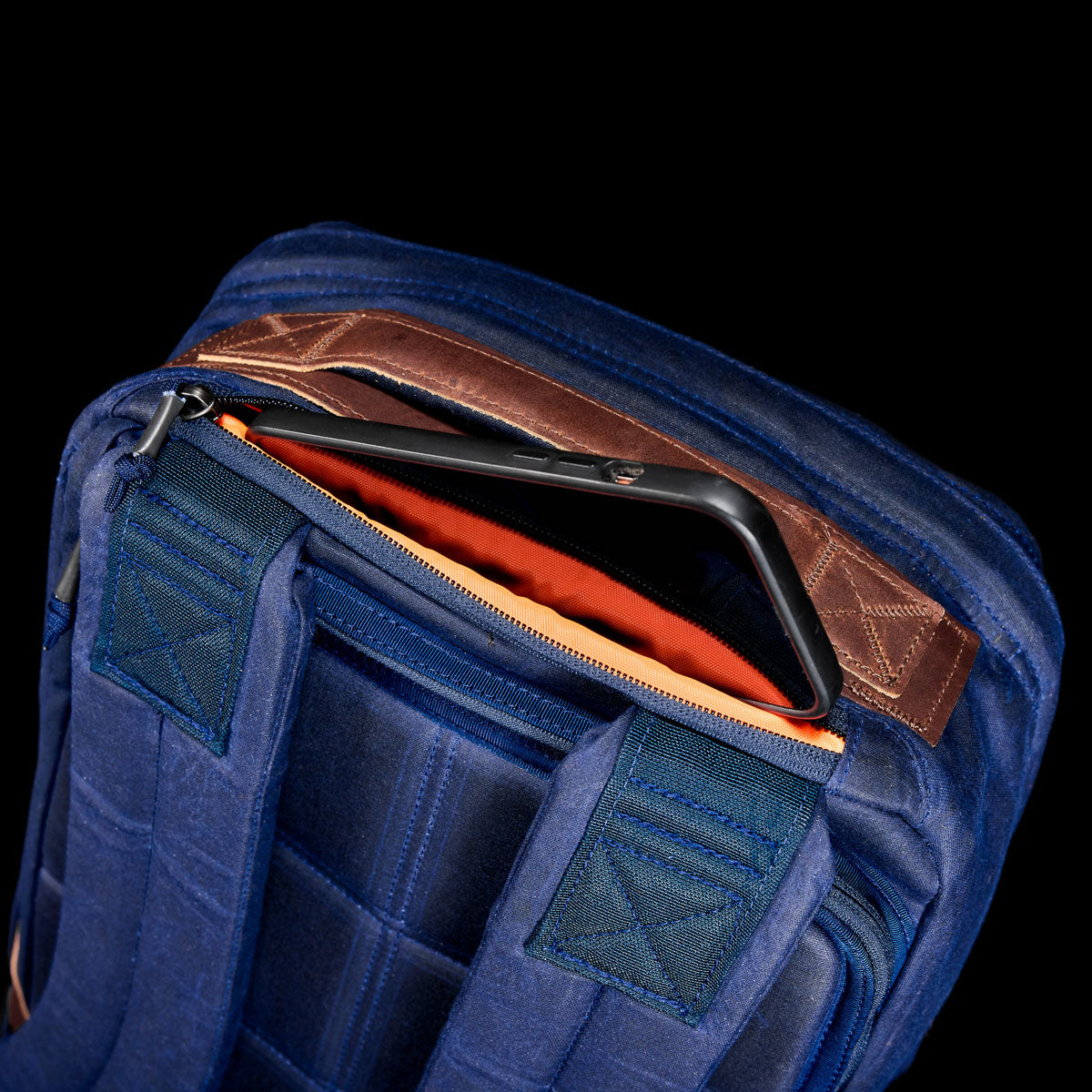 The GR1 USA - Heritage is a retro rucksack with blue waxed duck canvas and brown leather accents. It's partly unzipped, showing off an orange lining and a tablet inside, designed for style and durability.