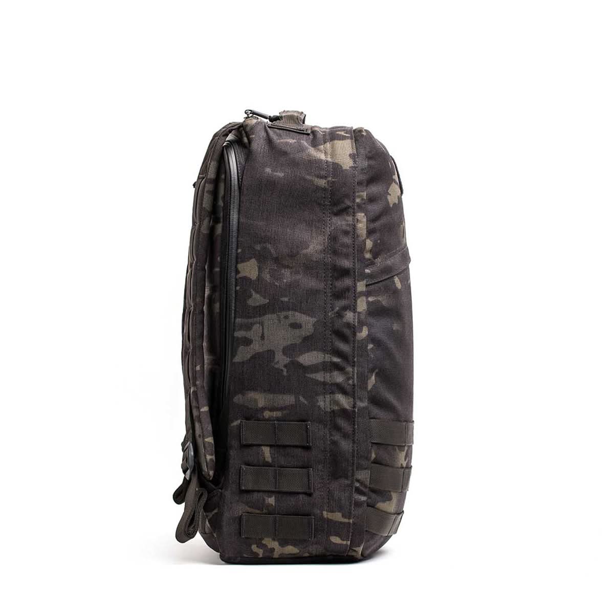 Side view of a black camouflage GR1 USA - Cordura (The Original Ruck) backpack made with Special Forces-grade materials and multiple straps, shown against a plain white background.