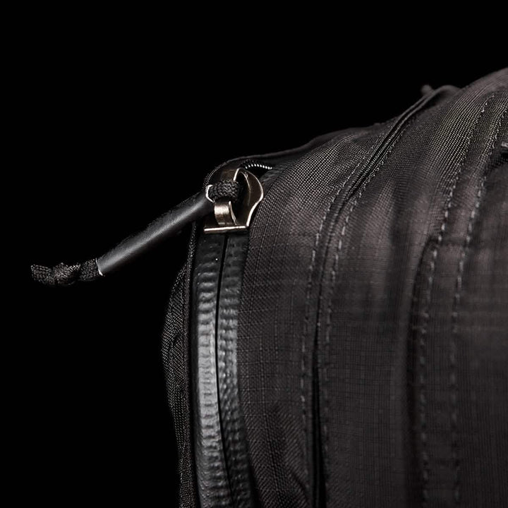 Close-up of the GR2 - Ripstop ROBIC® travel bag by GORUCK, featuring a slightly open zipper with a black cord attached to the pull. The fabric texture and stitching stand out against the dark background, emphasizing its water-resistant design.