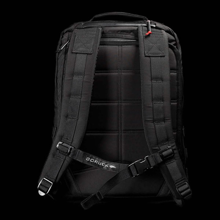 Displayed against a dark background is the GR2 - Ripstop ROBIC® rucksack in black, complete with padded shoulder straps and a chest strap. The back panel includes quilted padding for added comfort, while the GORUCK brand name is visible on the chest strap. This water-resistant travel bag combines style and practicality, making it an ideal companion for any journey.