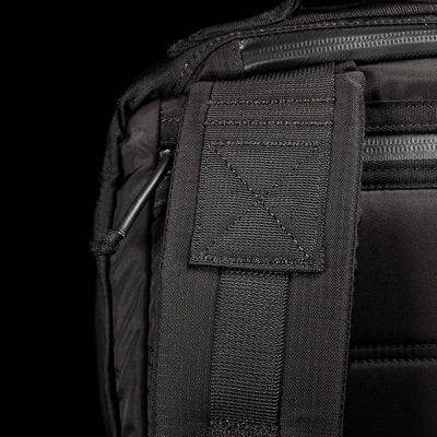 Close-up of the GR2 - Ripstop ROBIC® rucksack by GORUCK displaying detailed stitching and a padded strap. The texture of the fabric stands out, highlighting its water-resistant quality, with a partially visible metal clip. The dark background underscores the premium design and craftsmanship of this black travel bag.