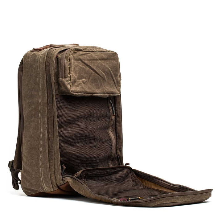 The GR2 - Heritage Waxed Canvas Backpack is shown with top and front compartments open, displaying mesh pockets and interior sections. Made from durable Waxed Duck Canvas for rugged style and lasting performance.