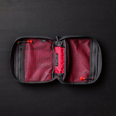 An open GR2 Field Pocket - GRXC2 Samurai 2.0, crafted from JPXDP fabric in black and red with mesh pockets and a zippered design, lies on a black surface.